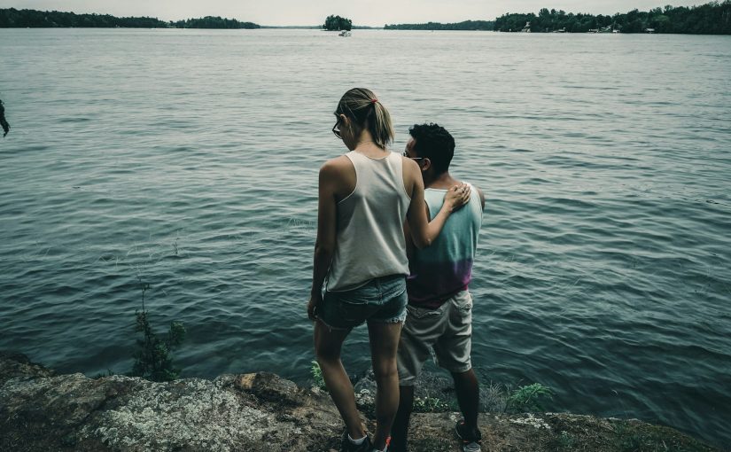 woman in white tank top and gray shorts standing on rocky shore during daytime